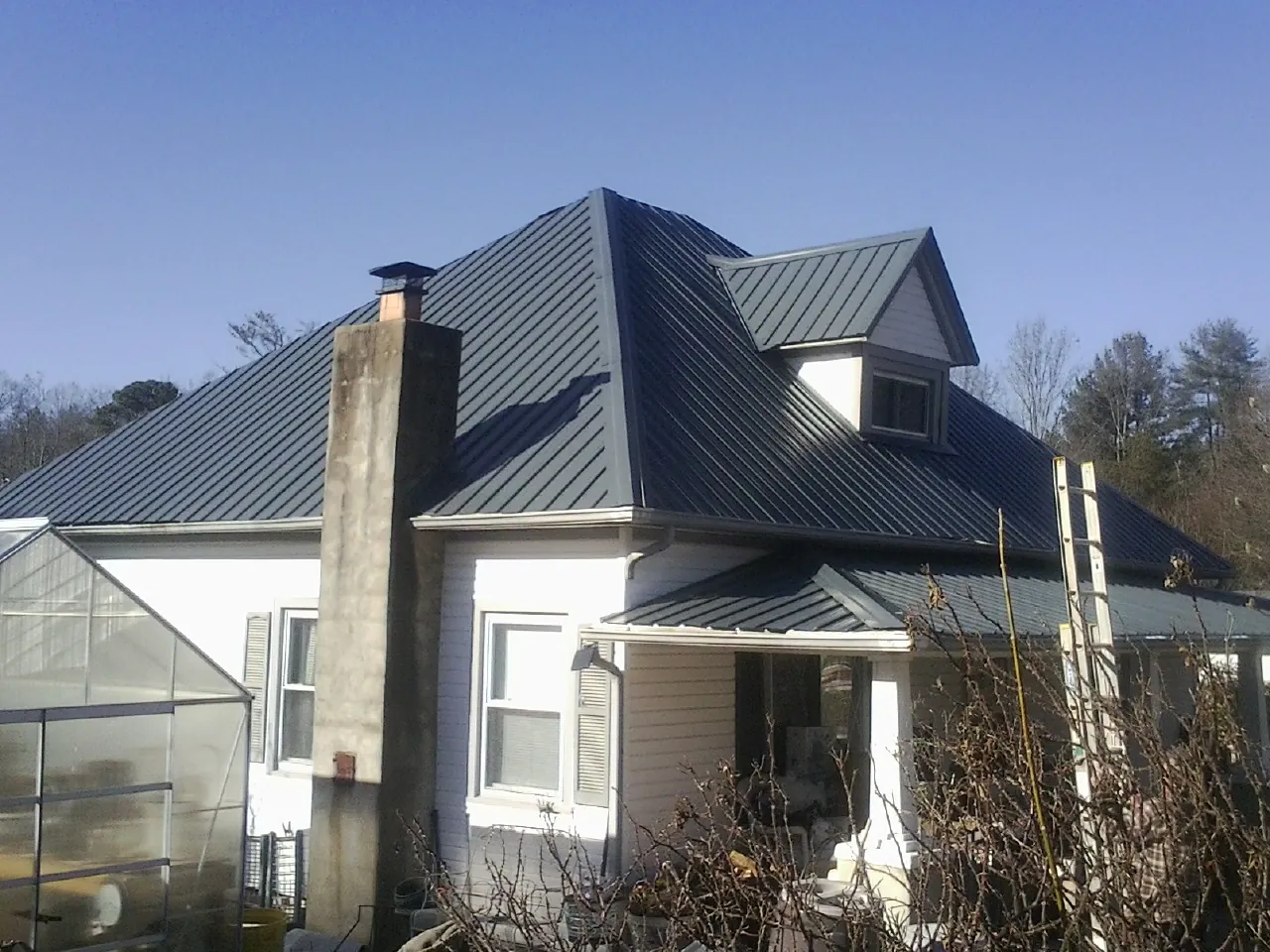 Dark blue standing seam metal roof on a white farmhouse with dormer — Slate & Tile Roof Repair by Roofing Brothers in Penfield