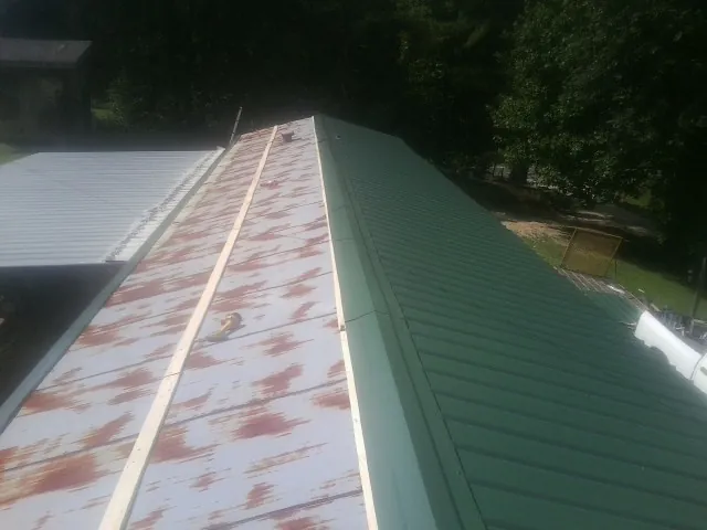 Old rusted panels beside newly installed green metal roofing — Wind Damage Roof Repair by Roofing Brothers in Penfield