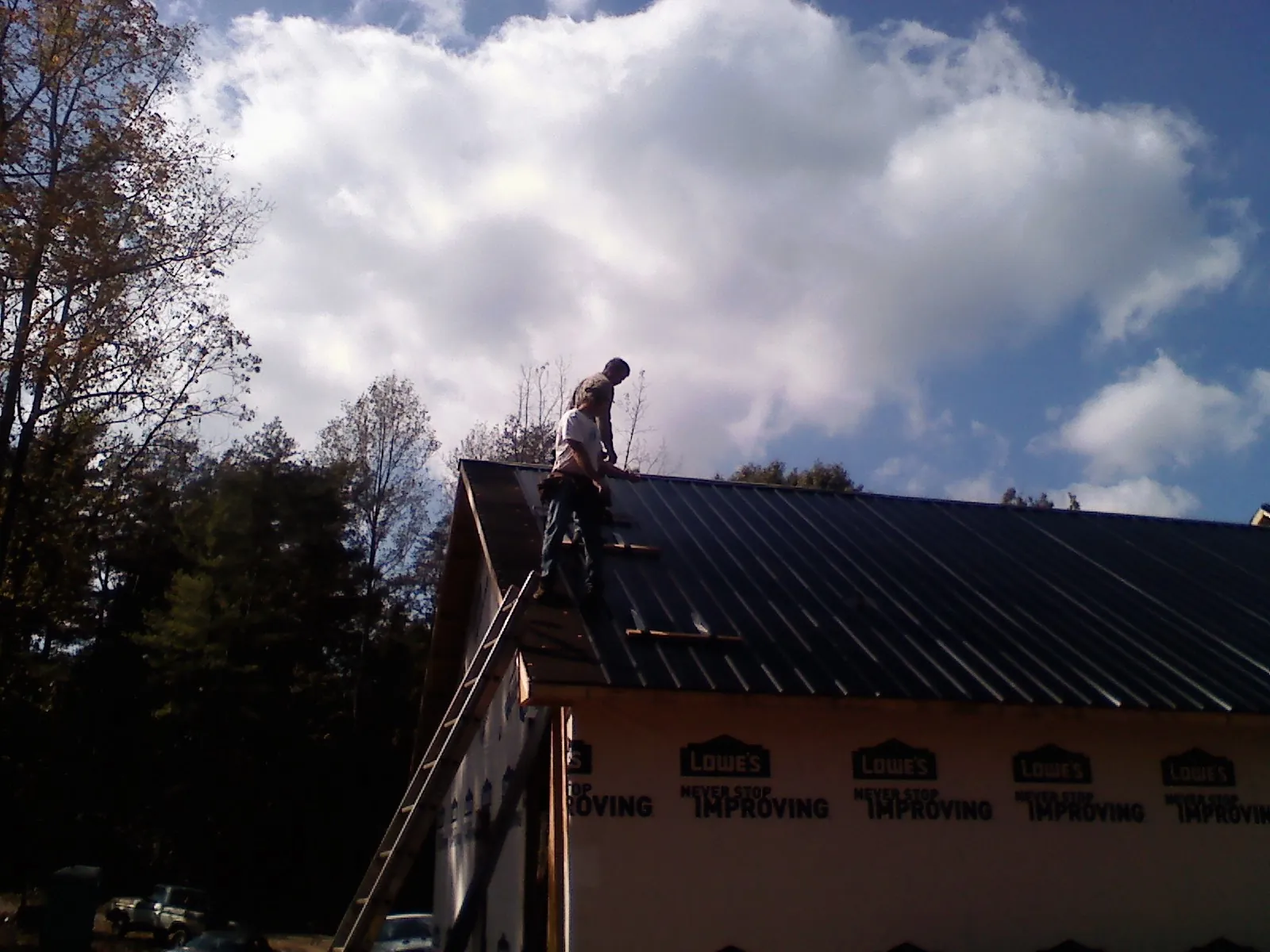 Roofer fastening dark metal panels high against a cloudy sky, from a Roof Inspection job in Penfield