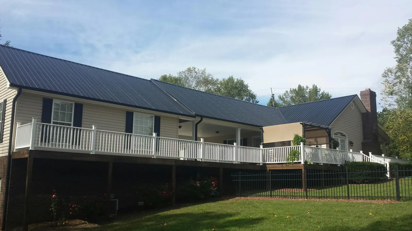 Black metal roof above a long white railed deck on a hillside home in Penfield